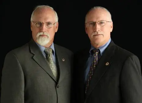 The Kennedy Twins - James Ronald and Walter Donald Kennedy The Kennedy Twins, James Ronald (Ron) Kennedy and Walter Donald (Donnie) Kennedy, wearing formal suits with serious expressions, posing against a black background.